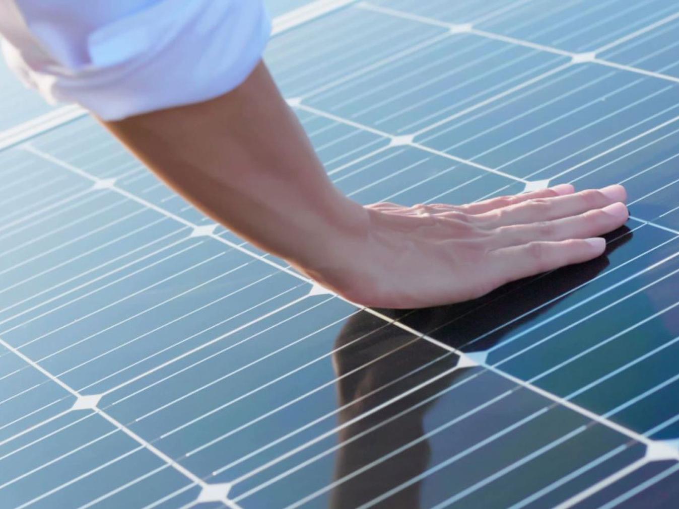Uma mão a tocar em módulos fotovoltaicos. 