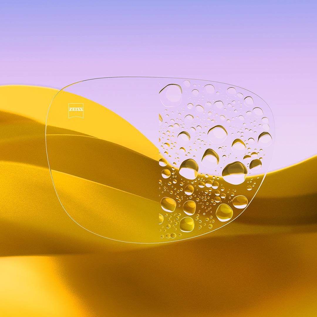 Uma lente dividida ao meio, com um lado nítido e limpo com ZEISS DuraVision Gold UV e um lado coberto de gotas de água.