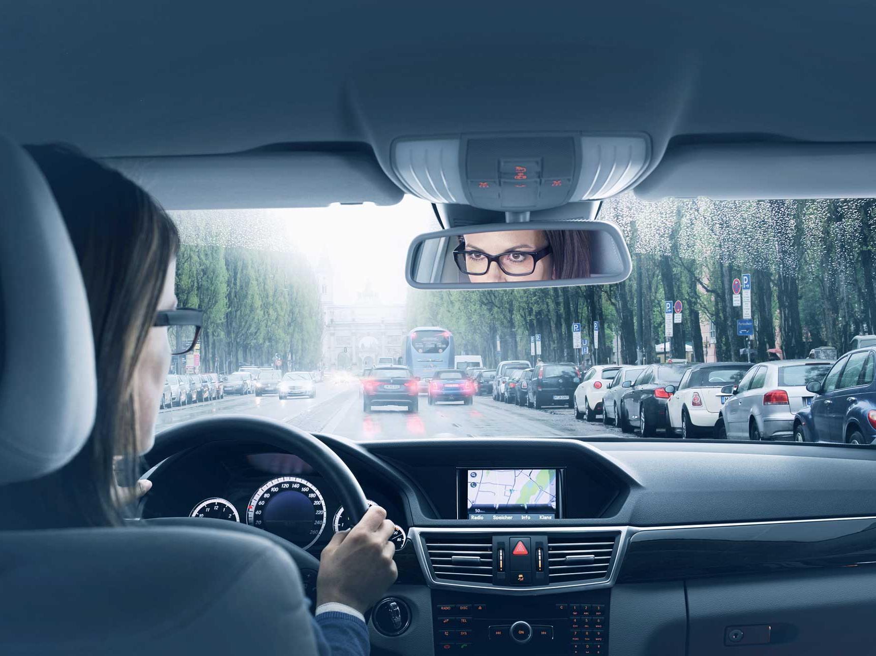 An image of a car interior with a woman sitting at the driver's seat. 