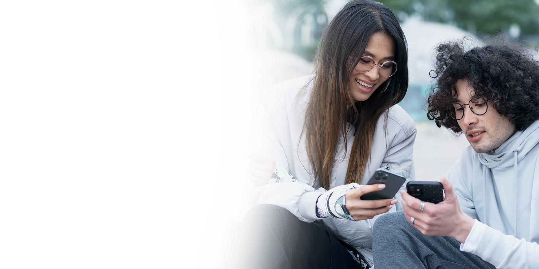 Dois jovens, uma mulher de cabelo castanho comprido a sorrir e um menino de cabelo preto encaracolado com óculos ZEISS SmartLife a olharem para os seus telefones. 