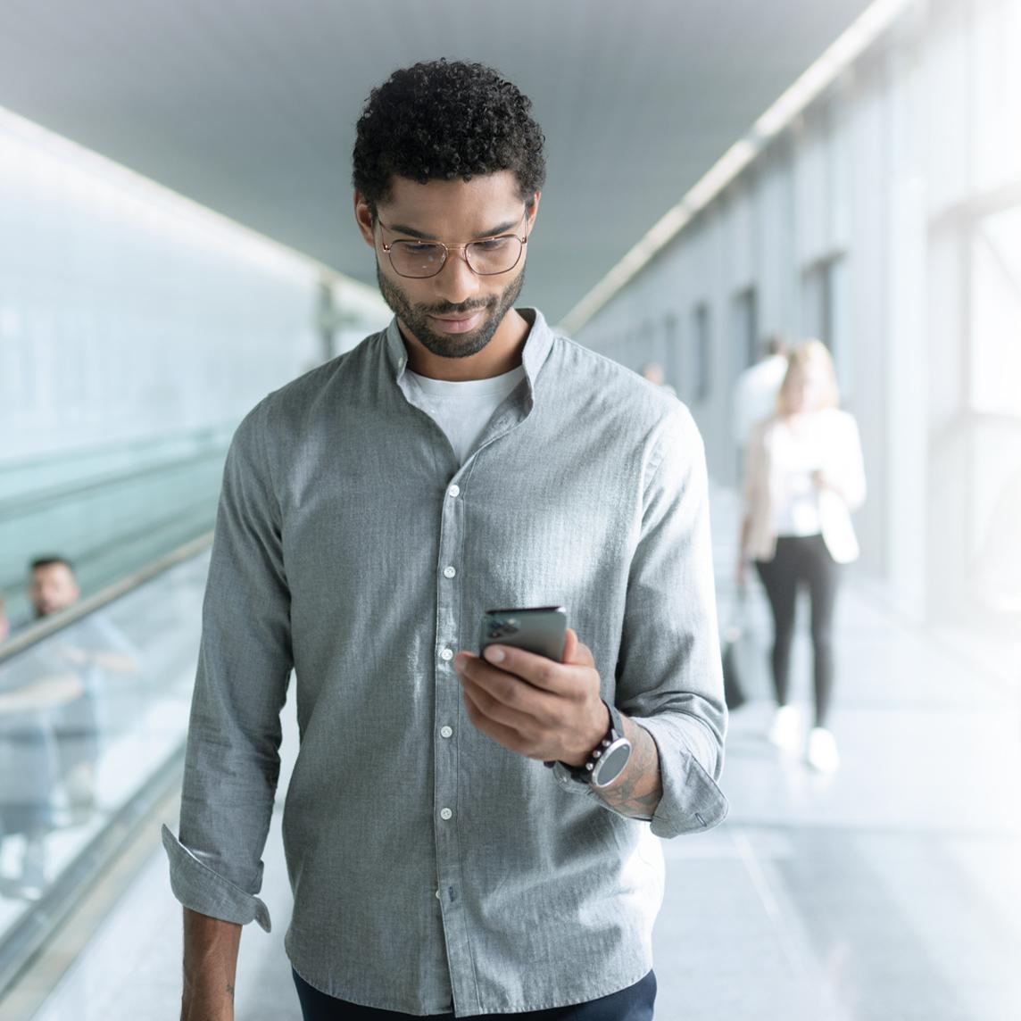 Um jovem com lentes ZEISS SmartLife a olhar para o telemóvel enquanto caminha.