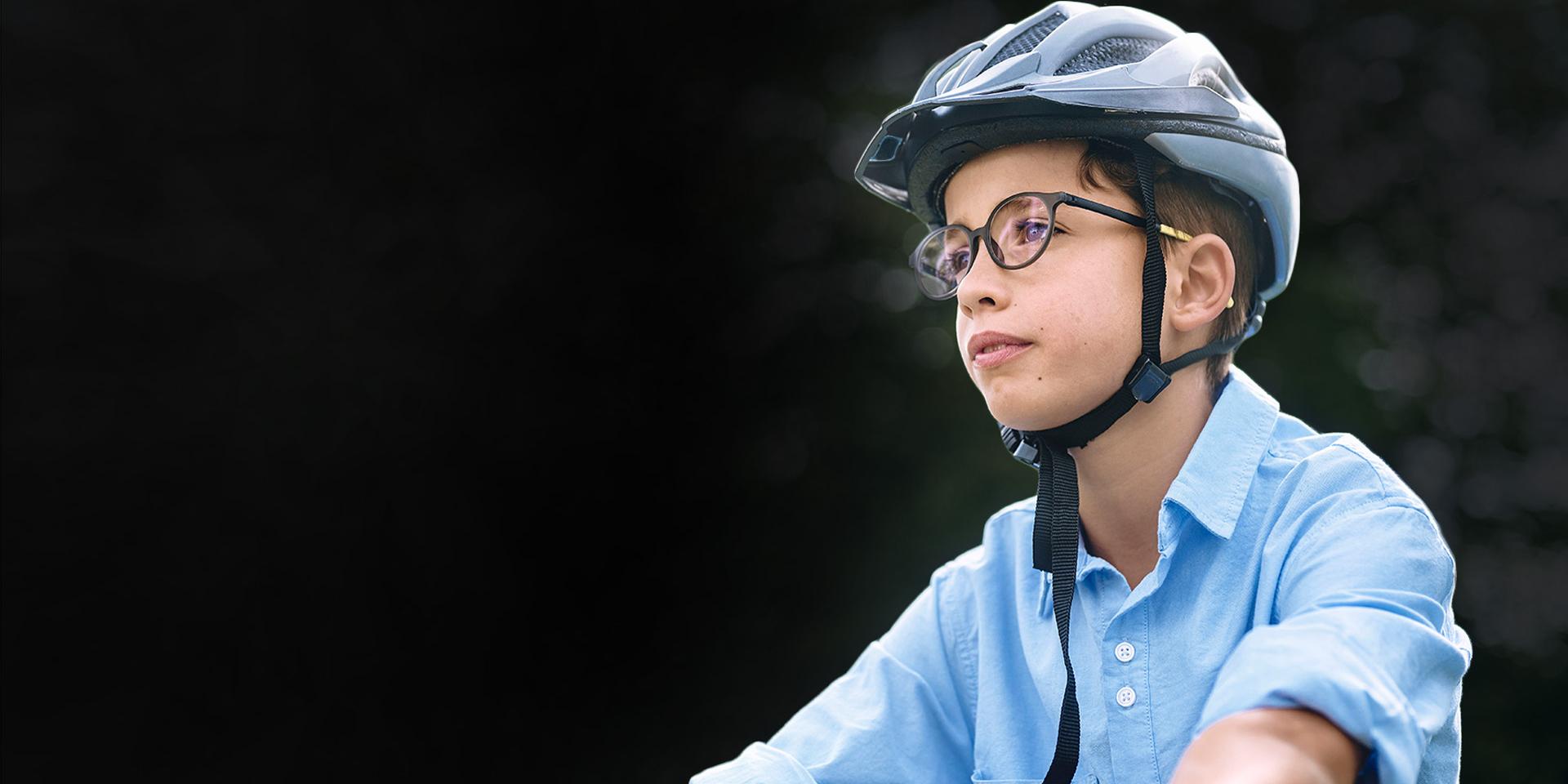 Um menino com óculos e capacete, aparentemente a andar de bicicleta.