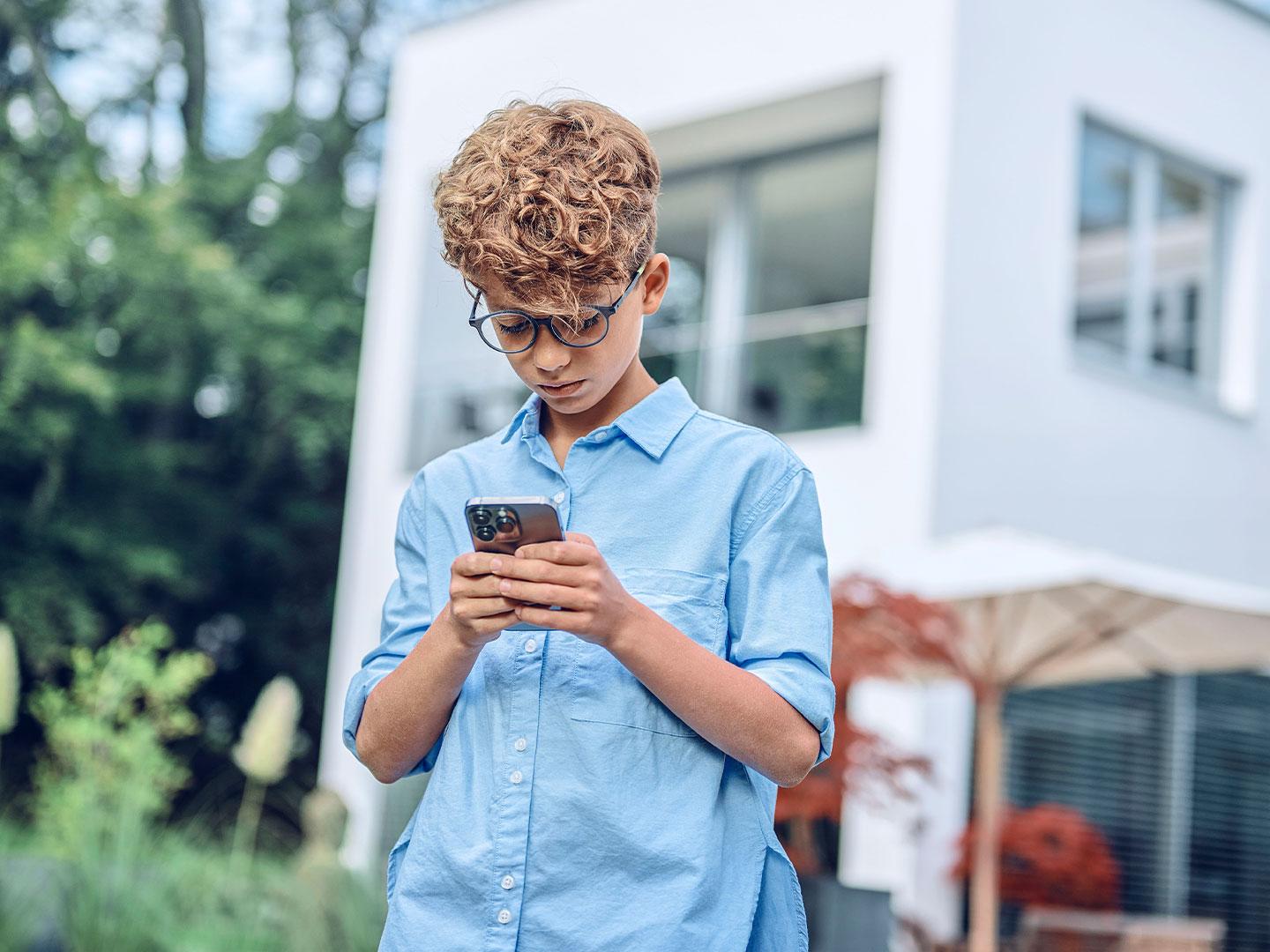 Jovem no exterior a olhar para o telemóvel.