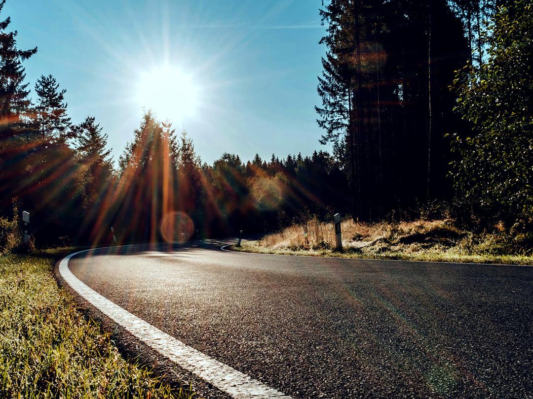 Uma imagem deslizante em que metade mostra uma estrada num bosque com luz brilhante do sol e a outra metade mostra a mesma estrada com brilho reduzido e contraste aumentado, destacando o efeito de lentes de óculos de sol polarizadas.