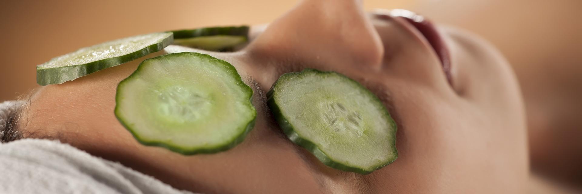 Mulher jovem com uma toalha na cabeça e rodelas de pepino nos olhos