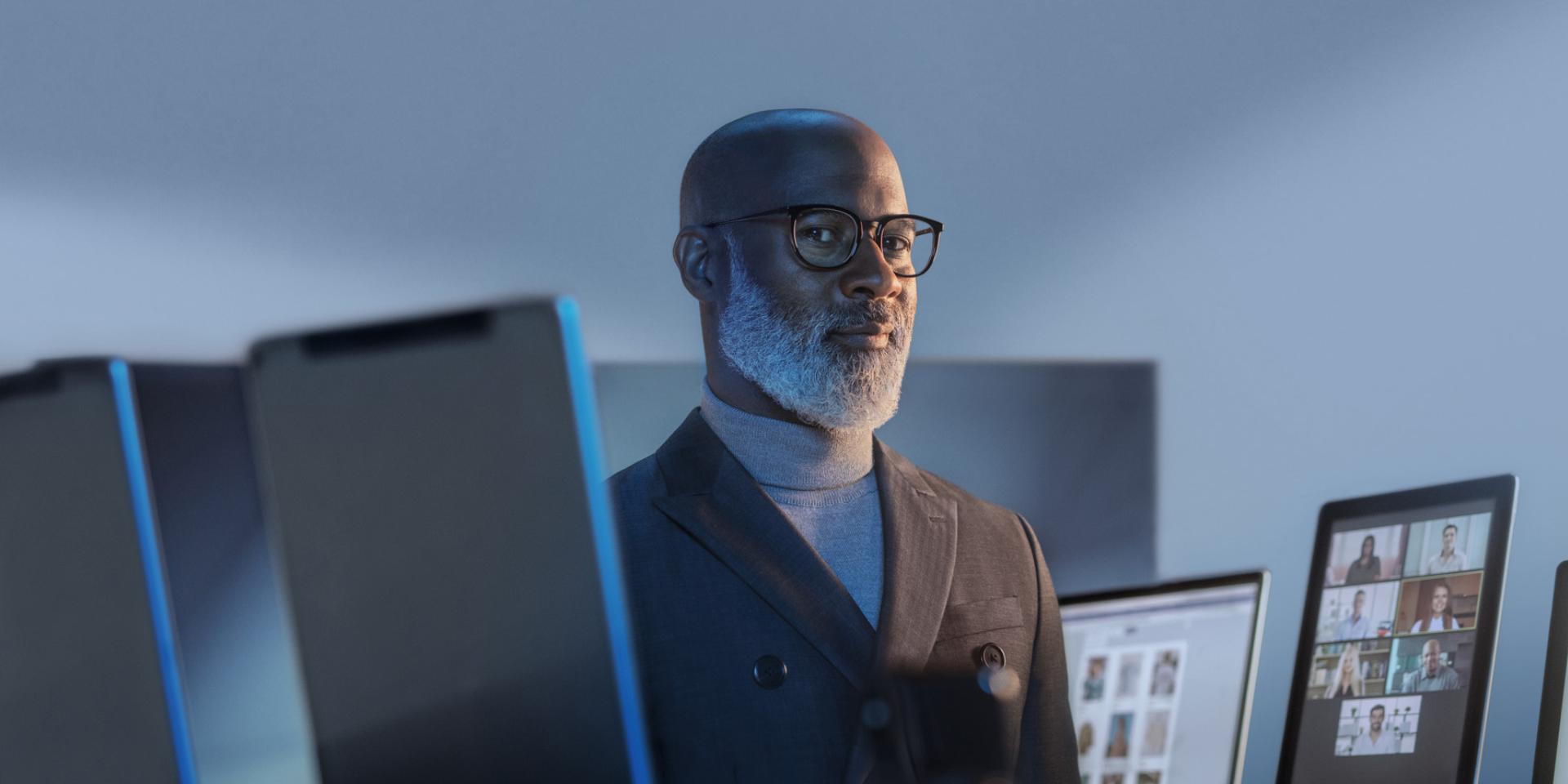 Homem sorridente rodeado de dispositivos digitais a usar óculos com ZEISS BlueGuard para proteção contra a luz azul.