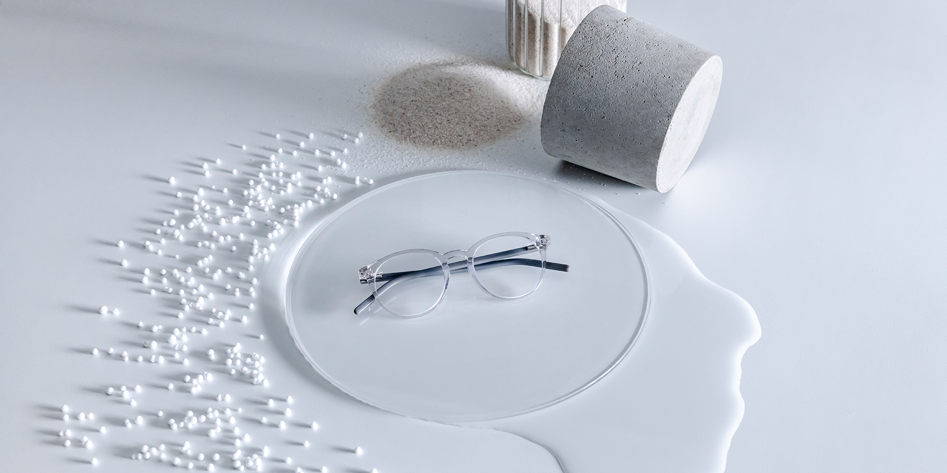 Óculos com lentes ZEISS com revestimento DuraVision® colocados numa base de vidro rodeada de água, areia, contas e uma pedra.