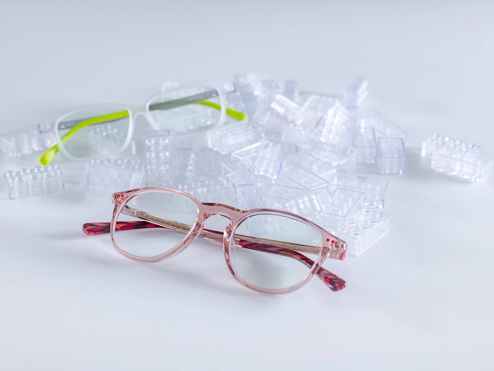 Dois pares de óculos para crianças com lentes ZEISS e revestimentos DuraVision® Kids. Os óculos estão posicionados entre tijolos de brincar transparentes.