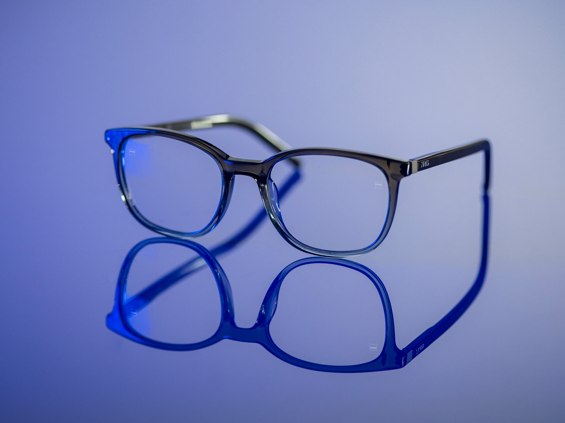 Óculos com lentes ZEISS com material BlueGuard, sobre um fundo de luz azulada. Apenas um reflexo azulado muito reduzido é visível nas lentes.