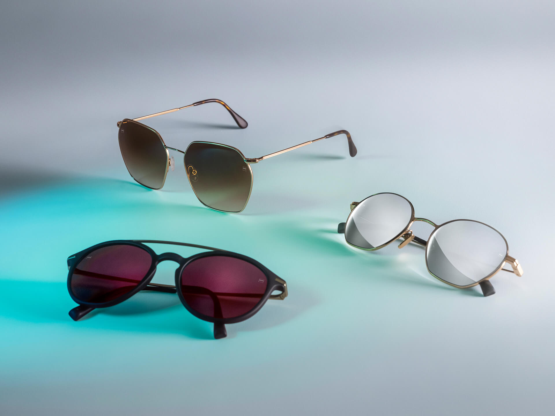 Três pares de óculos de sol com lentes ZEISS de cores diferentes, com revestimentos DuraVision Sun, DuraVision Mirror e Flash Mirror, sobre um fundo branco com reflexo de luz azul.