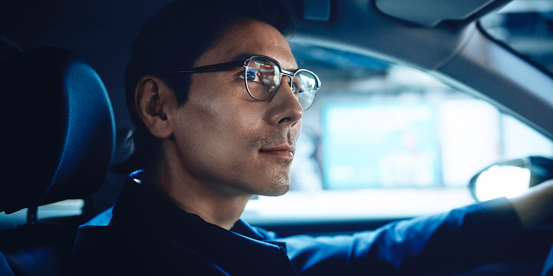 Homem a conduzir um carro, com um ar confiante e a esboçar um ligeiro sorriso. Está a usar lentes monofocais ZEISS DriveSafe.