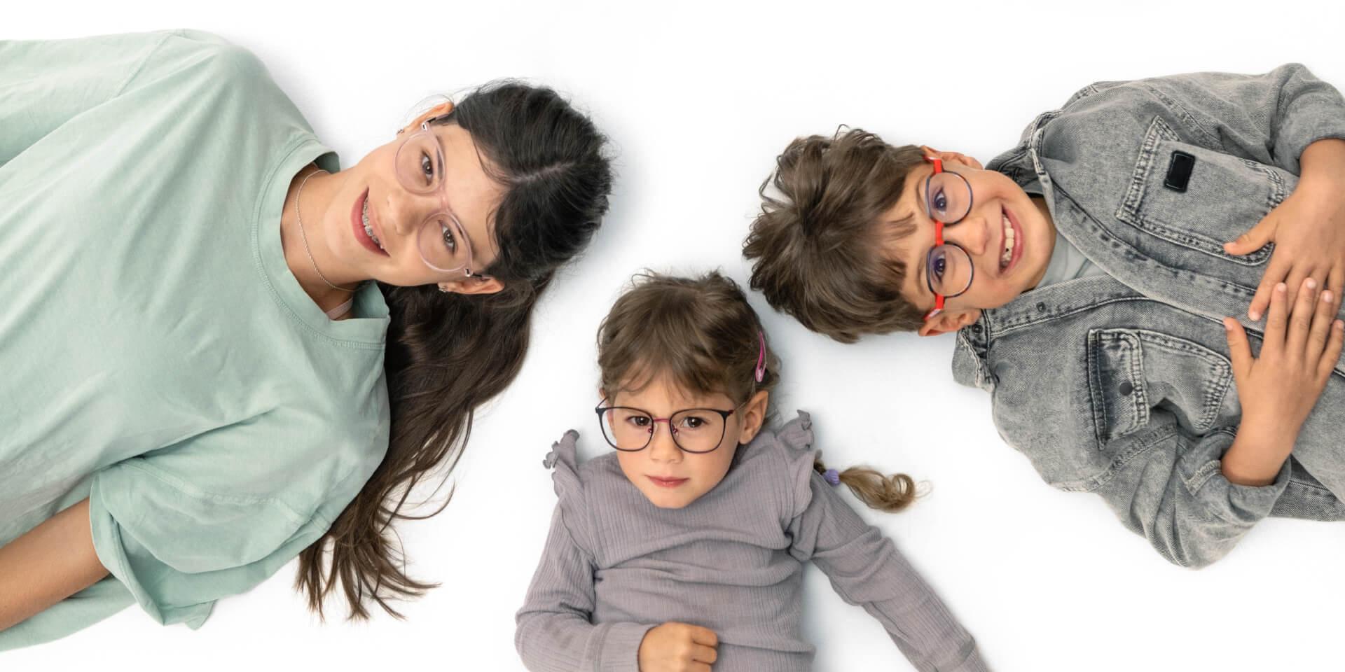 Uma adolescente e duas crianças deitadas no chão a usarem lentes ZEISS para a miopia.