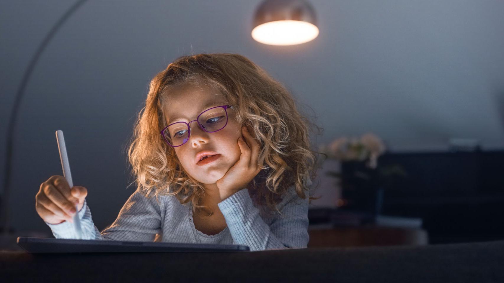 Menina numa sala de estar escura a olhar para um tablet.