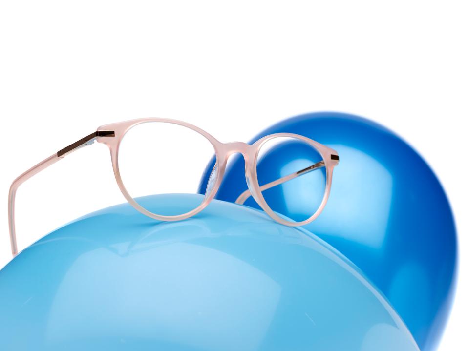 Óculos cor-de-rosa com lentes ZEISS MyoCare sobre um balão azul-claro.
