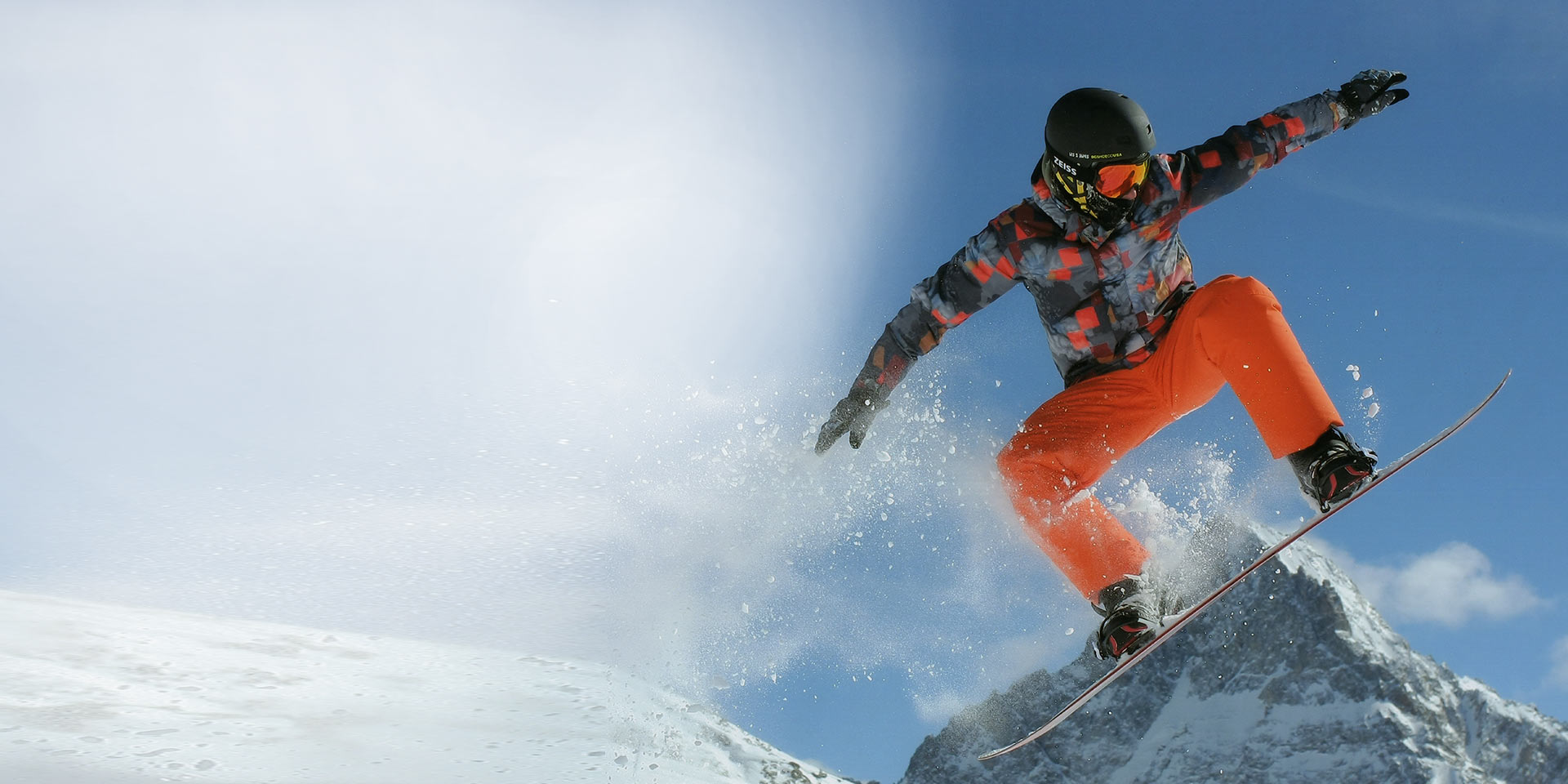 Homem a saltar numa prancha de snowboard, com capacete de esqui preto e máscara ZEISS para a neve com tecnologia Interchargeable para proteção