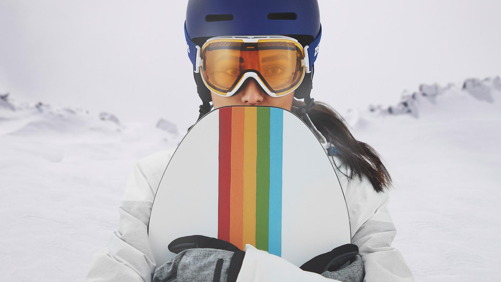 Jovem mulher a usar uma máscara de neve com a tecnologia ZEISS Interchangeable e a segurar uma prancha de snowboard.