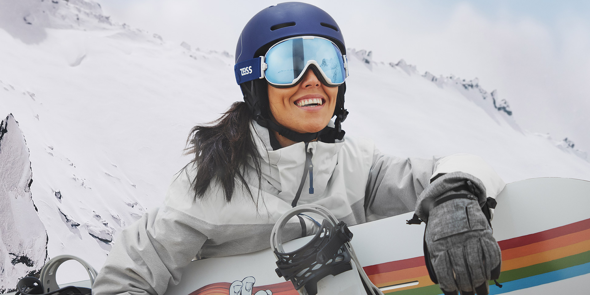 Jovem mulher a usar uma máscara de neve com a tecnologia ZEISS Interchangeable e a segurar uma prancha de snowboard.