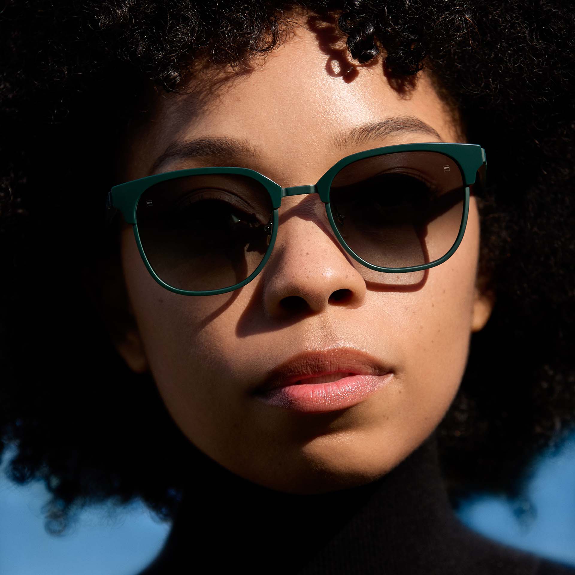 Mulher a usar uma armação verde com lentes com tonalidade degradê. 