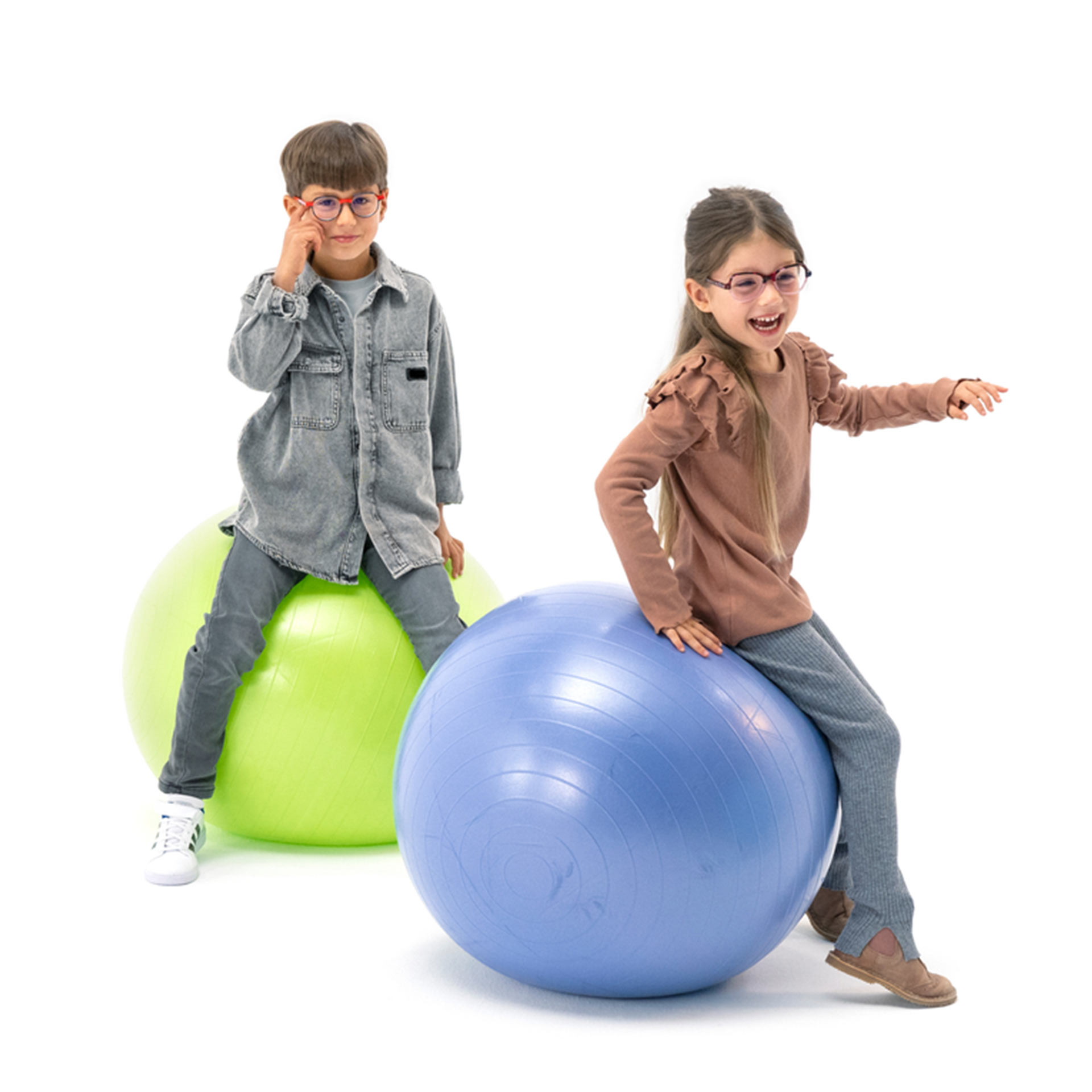 Um menino e uma menina, ambos de óculos, saltitam alegremente em bolas de ginástica.